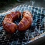A sausage on the grill with bacon wrapped around it.