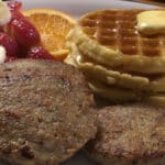 A plate of food with sausage, waffles and orange slices.